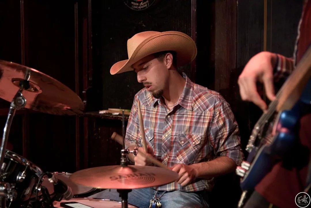 Batteur en chapeau de cowboy concentré derrière la cymbale, en spectacle